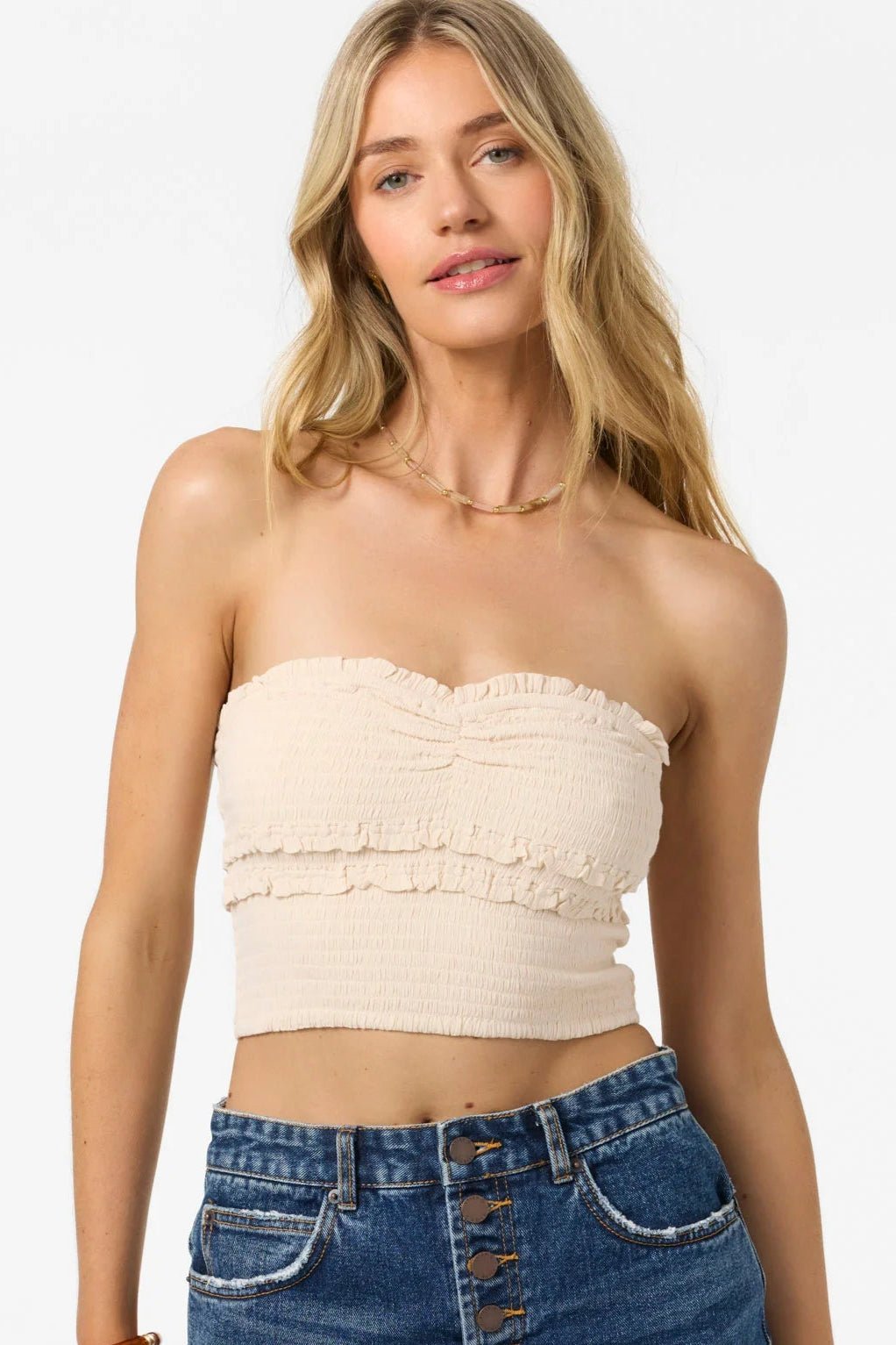 Woman wearing a beige strapless top and denim shorts on a white background